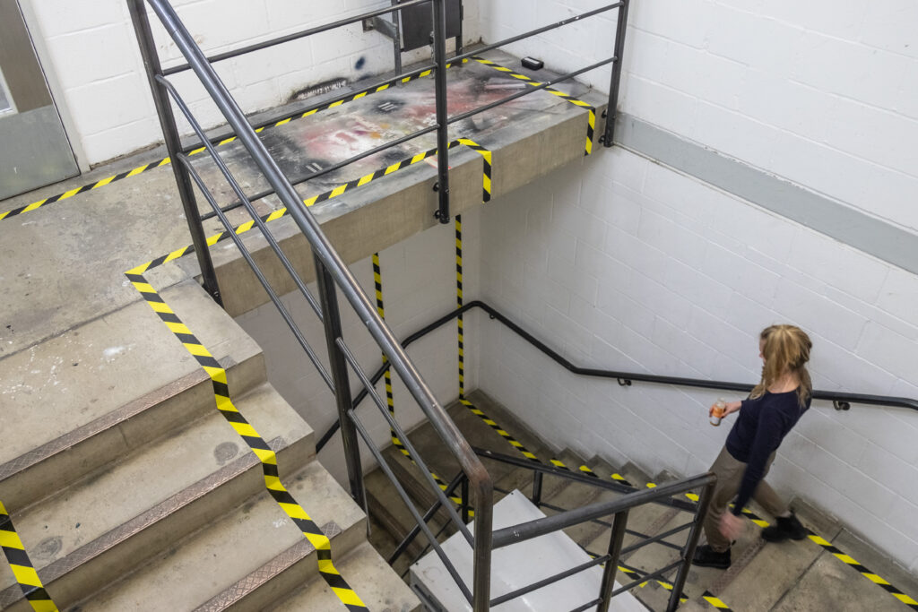 A woman walking down a staircase covered in hazard tape that runs up the wall to create an infinity loop.